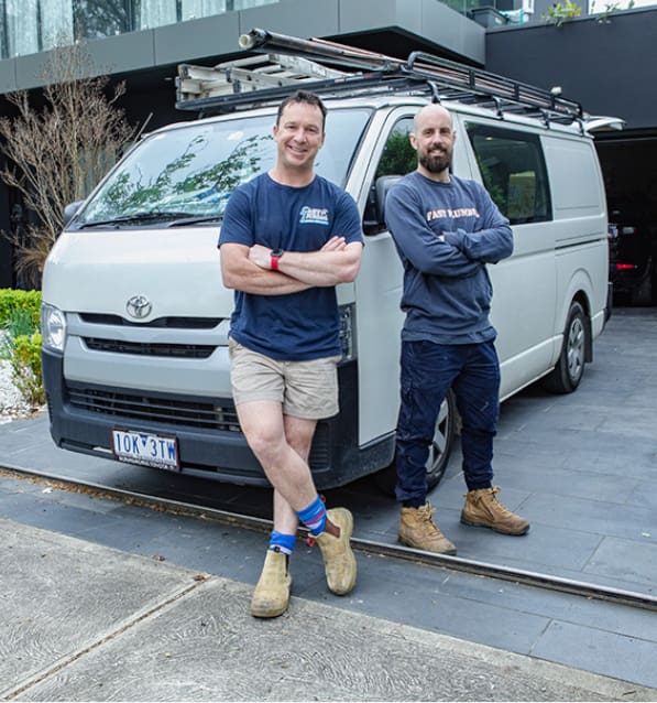 Friendly Melbourne plumber duo standing in front of their plumbing van